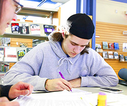 Deux étudiants blancs travaillant sur un devoir dans une bibliothèque postsecondaire