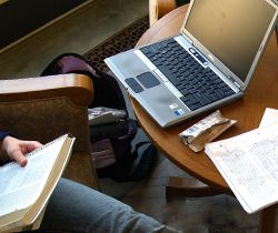 Étudiant lisant un livre avec un ordinateur portable sur une table