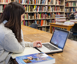 A white female post-secondary student working on an assignment at the library.
